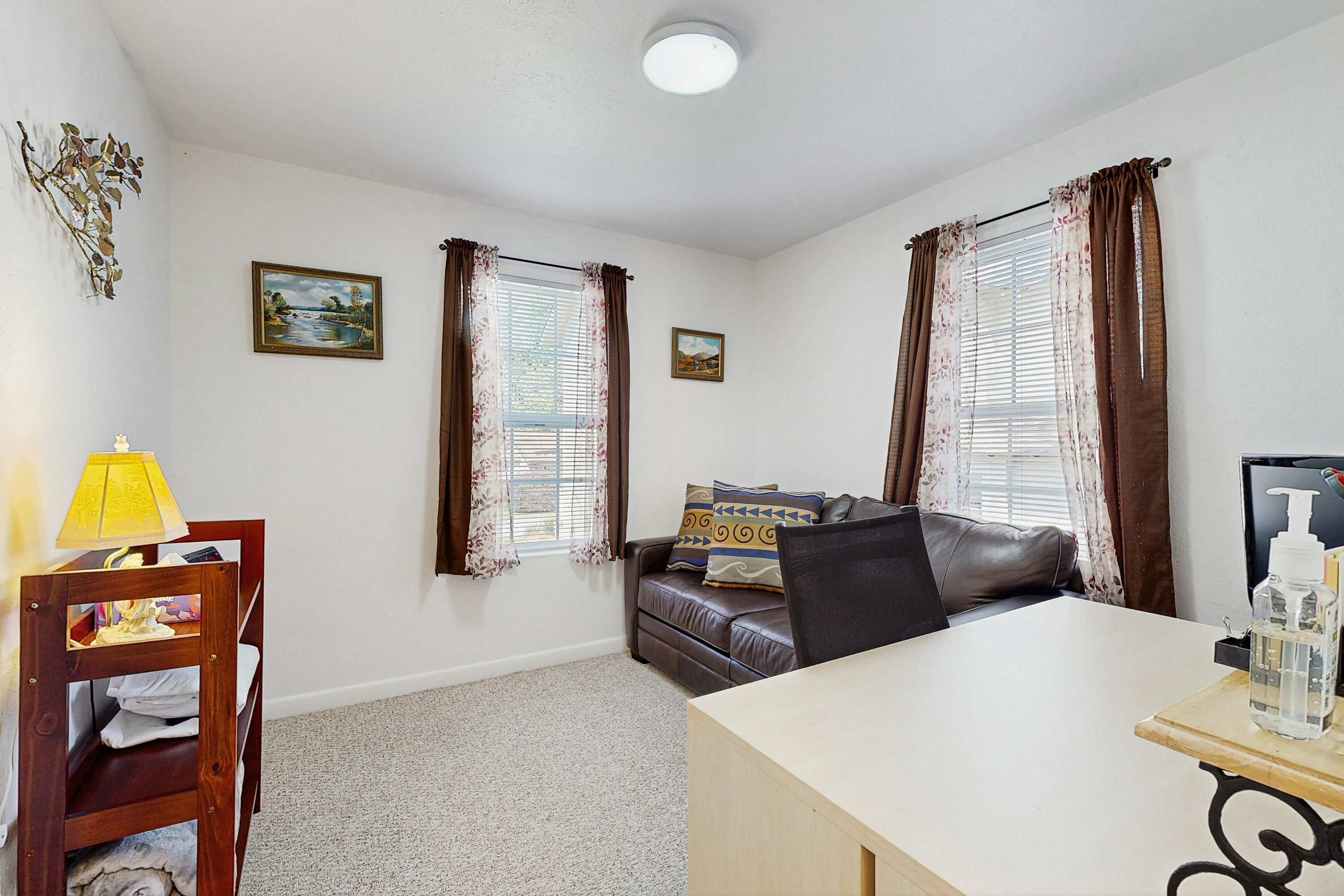 A room with a sofa, a table, a lamp, and two windows with curtains.