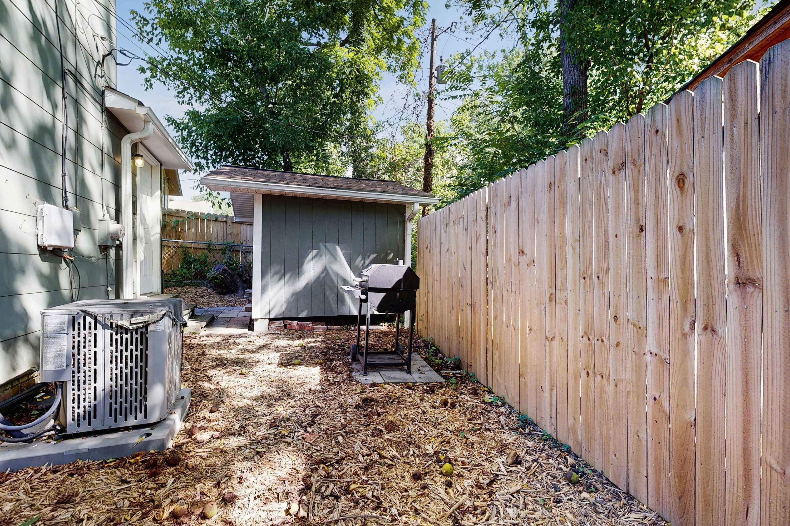 Un jardin avec une clôture en bois, un abri de jardin et un appareil de climatisation.