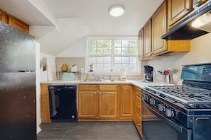 Una cocina con gabinetes de madera, lavavajillas empotrado, estufa y ventana con vista a árboles.