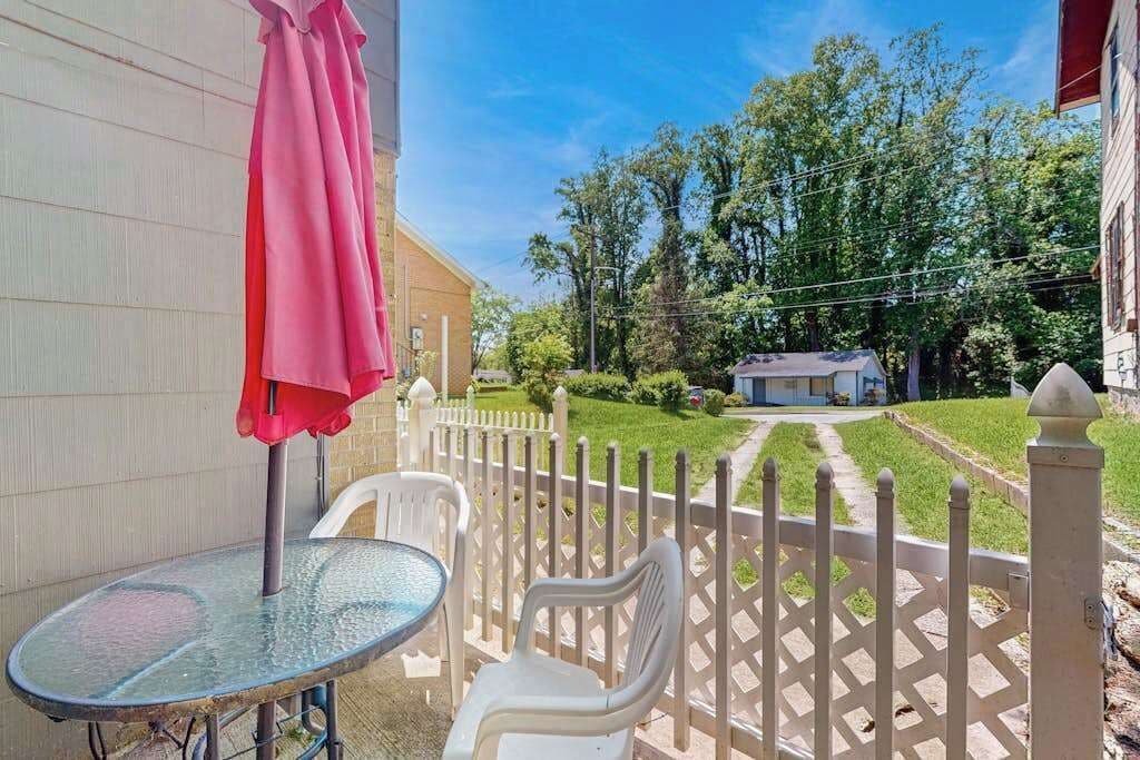 Une terrasse avec une table et des chaises en verre, une clôture blanche en bois et une maison en arrière-plan.