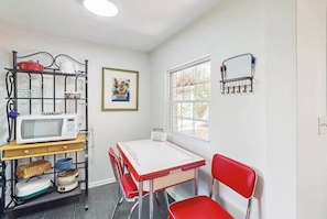 Une cuisine équipée d’un four à micro-ondes, d’une table, de chaises, d’une fenêtre et d’une étagère fixée au mur.