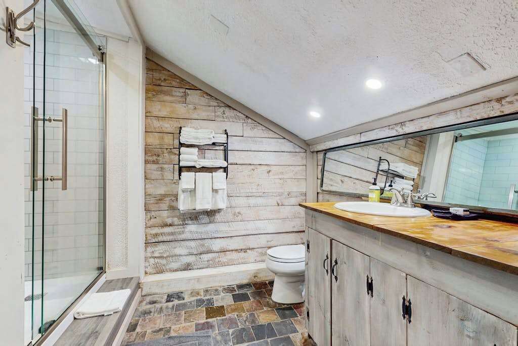 A bathroom with a glass shower, a wooden wall, a toilet, and a sink with a mirror.