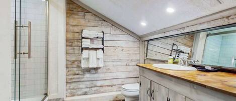A bathroom with a glass shower, a wooden wall, a toilet, and a sink with a mirror.
