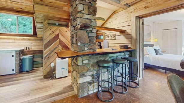 A rustic cabin interior with a stone fireplace, wooden walls, a bar area with stools, and a bed. - Scenic cabins with fireplaces, children's items, W/D - dog-friendly (Horse Shoe)