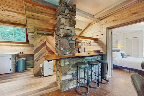 Ein rustikales Blockhaus-Interieur mit Kamin aus Stein, Holzwänden, einer Bar mit Hockern und einem Bett.