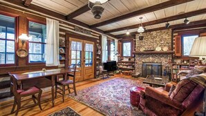 Ein gemütliches Blockhaus-Interieur mit einem Holzesstisch, Stühlen, einem Kamin, einer Couch und einem großen Teppich.