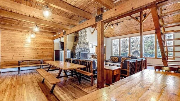A rustic wooden interior with exposed beams, a stone fireplace, and large windows. - Spacious Black Mountain cabin with game room, wood fireplace, firepit, & W/D (Black Mountain)