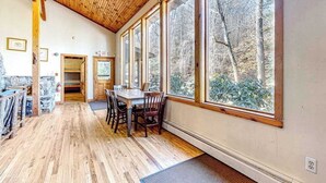 A wooden interior with a dining area, large windows, and a stone wall. - Spacious Black Mountain cabin with game room, wood fireplace, firepit, & W/D (Black Mountain)