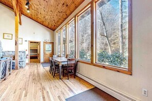A wooden interior with a dining area, large windows, and a stone wall.