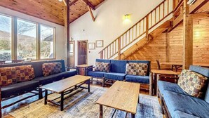 A spacious living area with a wooden staircase, large windows, and a blue sofa set. - Spacious Black Mountain cabin with game room, wood fireplace, firepit, & W/D (Black Mountain)