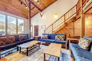 A spacious living area with a high ceiling, wooden beams, a blue sofa set, and a staircase.