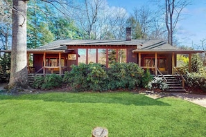 A rustic cabin with a covered porch, a chimney, and a well-maintained lawn.