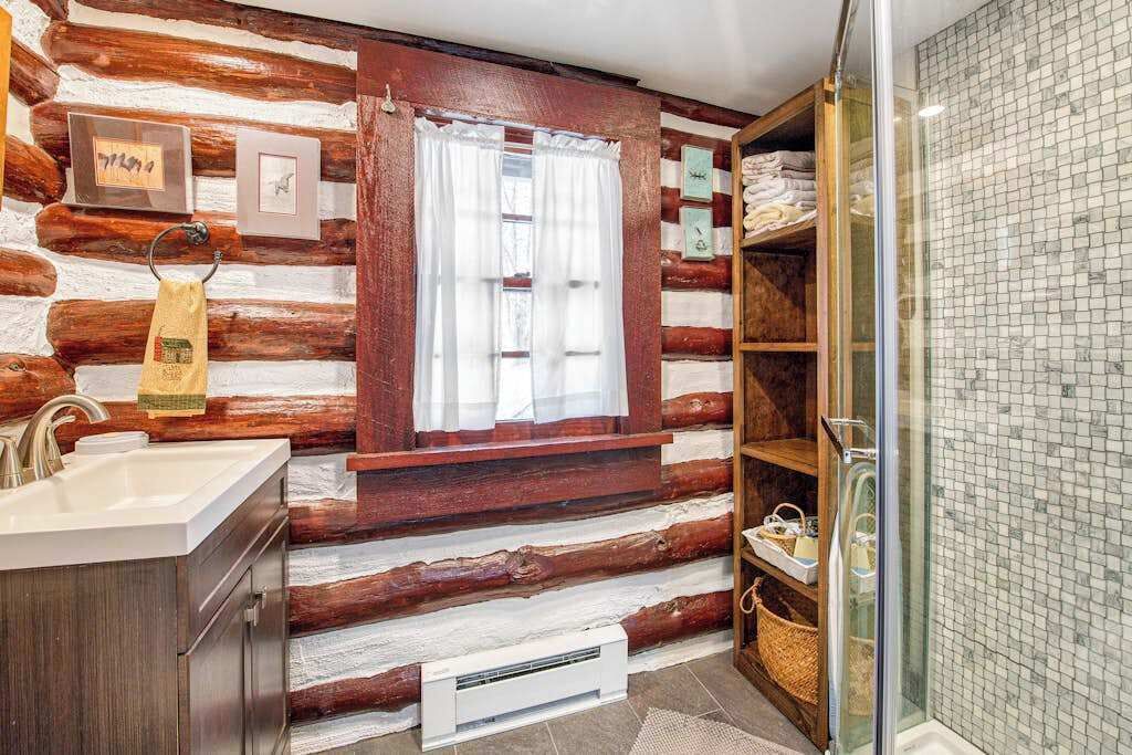 Ein Badezimmer in einer Blockhütte mit Waschbecken, Fenster, Handtuchhalter und Duschbereich.