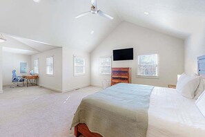 Ein Schlafzimmer mit einem Bett, einem Schreibtisch, einem Stuhl, einem Fernseher und einem Deckenventilator.