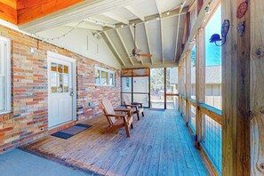 Eine überdachte Veranda mit Holzstühlen, einer Tür und einer Backsteinmauer.