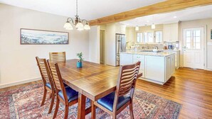 Un coin repas avec une table et des chaises en bois, une cuisine en arrière-plan et un tapis à motifs sur le sol.