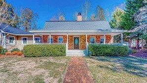 Une maison à deux étages avec une façade en briques, un porche à l’avant et un chemin menant à l’entrée.