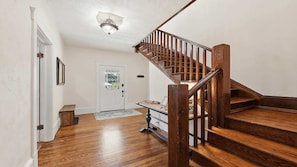 Eine Holztreppe führt zu einer zweiten Etage, eine weiße Tür mit Fenster und ein kleiner Tisch mit Teppich im Vordergrund.