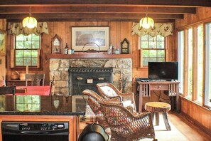 Ein rustikales Interieur mit Kamin aus Stein, Korbsesseln, einem Fernseher und Holzwänden.