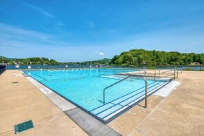 Ein rechteckiger Pool mit bepflastertem Rand, Metall-Geländern und blauem Himmel im Hintergrund.