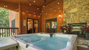 A hot tub on a wooden deck with stone walls and a stone fireplace. - Cozy yet Spacious – Game Room – Double-sided Fireplace (Pigeon Forge)