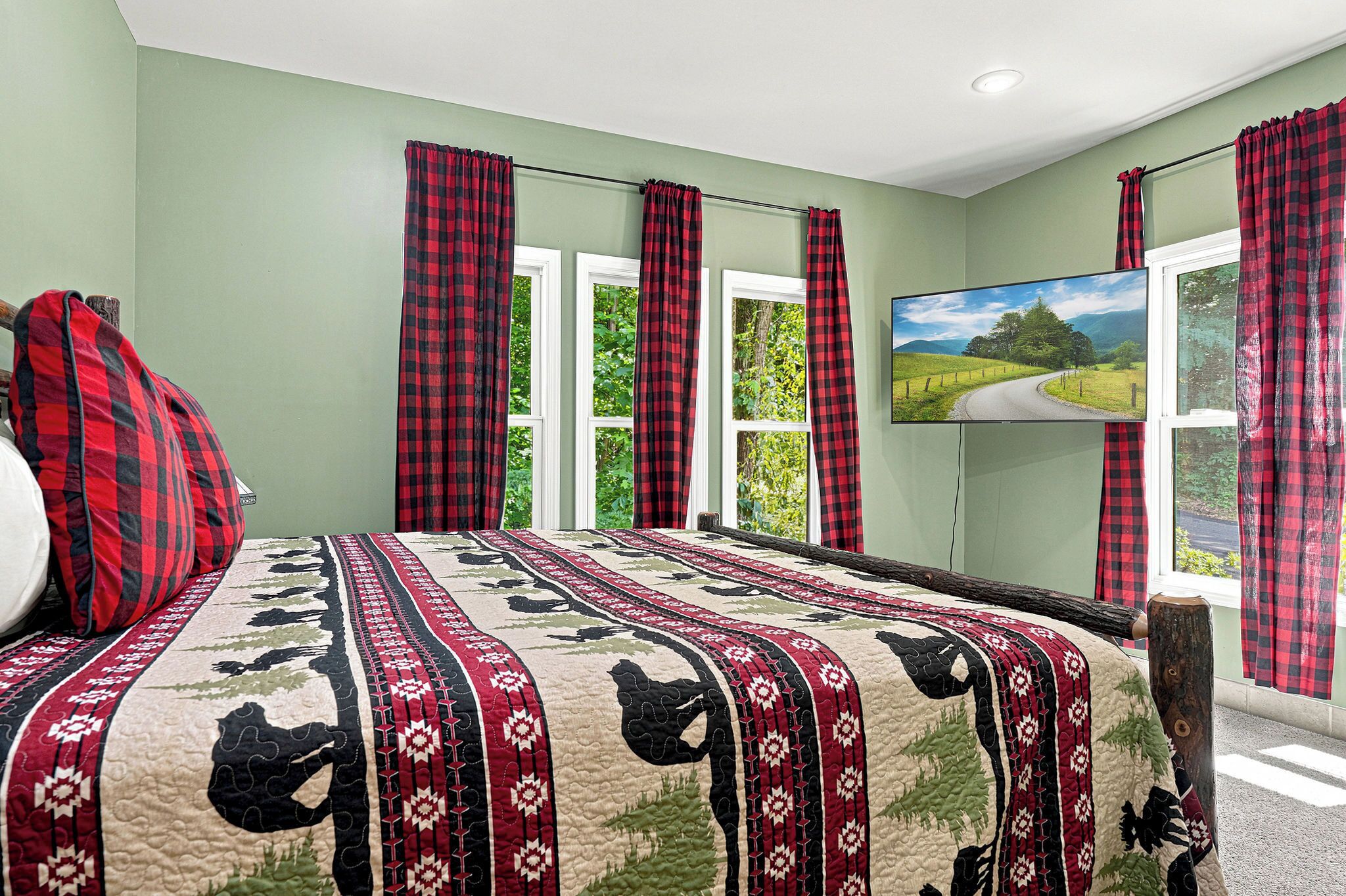 A bedroom with a bed, a television, and a window with curtains.