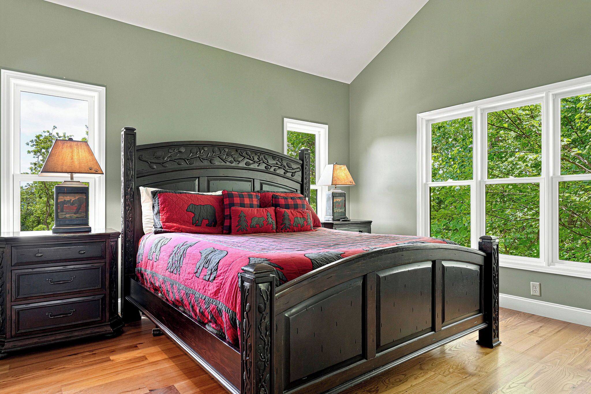 A bedroom with a large bed, two bedside tables, and a window with a view of trees.