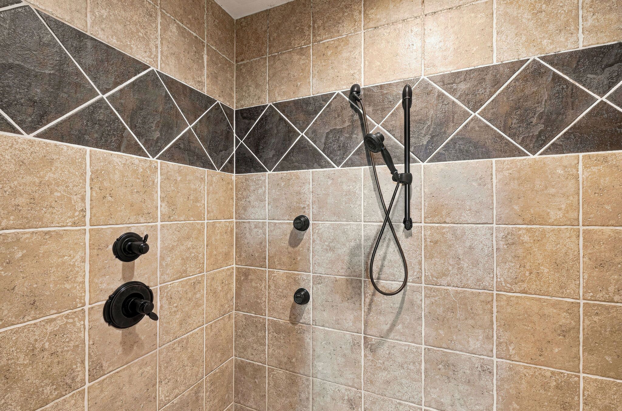A shower area with tiled walls, a showerhead, and a handheld shower attachment.