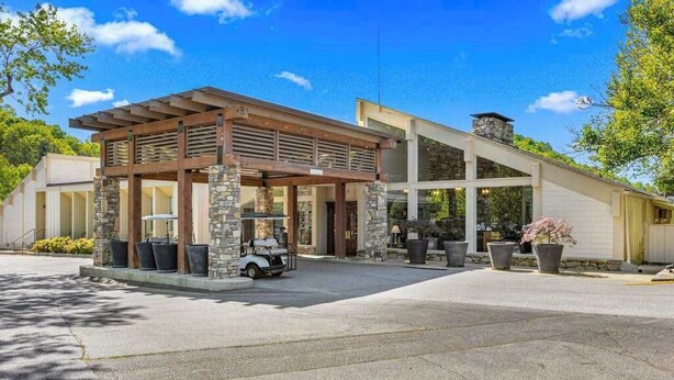 Un bâtiment moderne doté d’un patio couvert, de piliers en pierre et d’un véhicule garé devant.