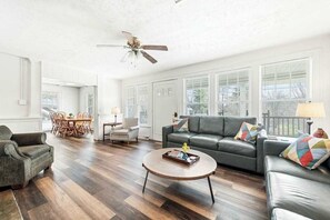 A spacious living room with a dark leather sofa, a round coffee table, and a dining area with wooden chairs. - Junaluska Lodge (Lake Junaluska)