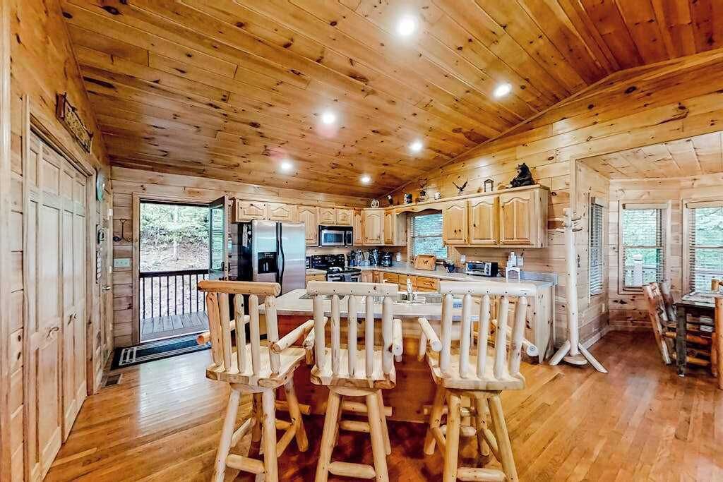 L’intérieur d’un chalet en bois comprend une cuisine, un coin bar et une vue sur l’extérieur, visible à travers la porte.