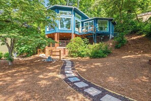 Ein modernes Haus mit einer großen Terrasse, umgeben von Bäumen und einem Steinweg.