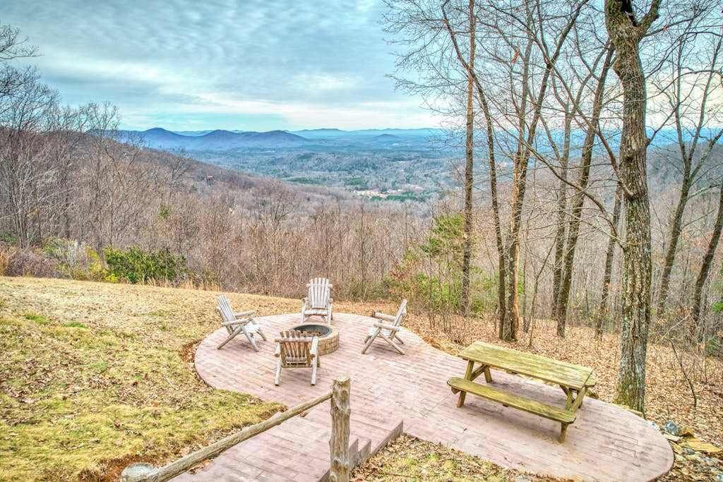 Un espace extérieur circulaire aménagé avec des fauteuils Adirondack et un banc en bois, le tout entouré d’une terrasse en bois.