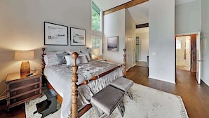 A bedroom with a large bed, a wooden headboard, a nightstand, a bench, and framed pictures on the wall. - Mountain gem w/pool,golf, hot tub, tennis, beach, wellness center - dog-friendly (Lake Lure)