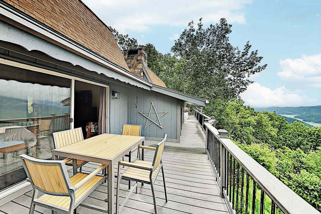 A wooden deck with a table and chairs, a railing, and a view of a forested area.