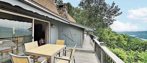 A wooden deck with a table and chairs, a railing, and a view of a forested area.