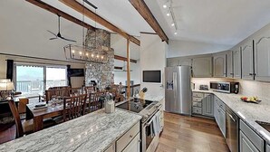 A modern kitchen with a stone accent wall, wooden beams, and a large island with seating. - Mountain gem w/pool,golf, hot tub, tennis, beach, wellness center - dog-friendly (Lake Lure)