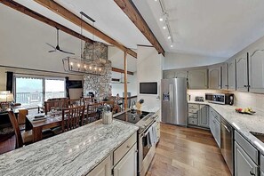 A modern kitchen with a stone accent wall, wooden beams, and a large island with seating. - Mountain gem w/pool,golf, hot tub, tennis, beach, wellness center - dog-friendly (Lake Lure)