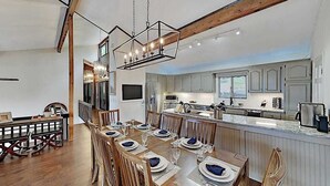 A spacious dining area with a long wooden table set for a meal, a kitchen with modern appliances, and a large island with a sink. - Mountain gem w/pool,golf, hot tub, tennis, beach, wellness center - dog-friendly (Lake Lure)