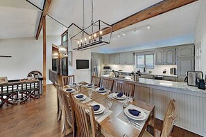 A spacious dining area with a long wooden table set for a meal, a kitchen with modern appliances, and a large island with a sink. - Mountain gem w/pool,golf, hot tub, tennis, beach, wellness center - dog-friendly (Lake Lure)