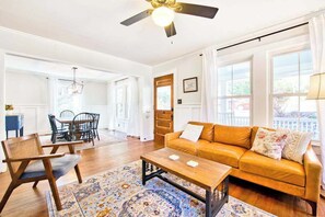 A living room with a sofa, coffee table, and chairs, a ceiling fan, and large windows. - Spacious dog-friendly Montreat cottage with firepit, mountain views, & patio (Montreat)