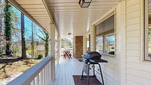 Une véranda couverte avec un barbecue, un mur en briques et une vue sur les arbres et une maison.