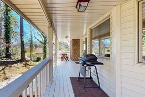 A covered porch with a grill, a brick wall, and a view of trees and a house. - Junaluska Gem (Lake Junaluska)