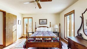Une chambre à coucher avec un lit en bois, un ventilateur de plafond, une table de chevet, une commode et un grand miroir.