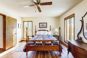 A bedroom with a wooden bed, a ceiling fan, a nightstand, a dresser, and a large mirror. - Junaluska Gem (Lake Junaluska)