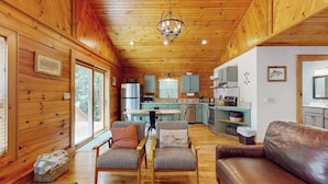 A cabin interior with wooden walls, a dining area, kitchen, and a living room with a sofa and chairs. - Happy Top Hideaway (Bryson City)
