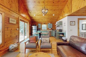 A cabin interior with wooden walls, a dining area, kitchen, and a living room with a sofa and chairs. - Happy Top Hideaway (Bryson City)
