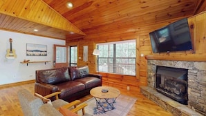 A wooden interior with a leather sofa, a television mounted on the wall, and a stone fireplace. - Happy Top Hideaway (Bryson City)