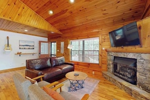 A wooden interior with a leather sofa, a television mounted on the wall, and a stone fireplace. - Happy Top Hideaway (Bryson City)