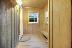 Un pasillo interior de madera con una ventana, una puerta y una alfombra pequeña en el suelo.
